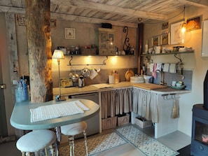 A rustic kitchen with a wooden table, stools, a hanging light fixture, and a stove. - Provençal apartment near Saint-Paul de Vence (Roquefort-les-Pins)