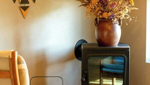 Ein Zimmer mit einem Holzhocker, einem Wanddekor, einer Vase mit Blumen und einem schwarzen Herd.
