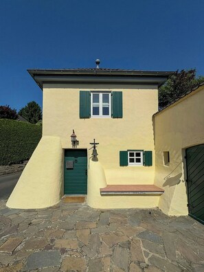 A two-story building with a green door, a small window with green shutters, and a bell above the door.