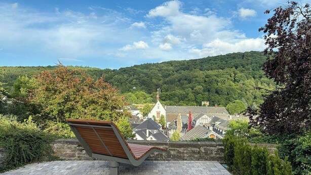 A bench overlooking a town with traditional architecture and a forested hill in the background. - Tower house with two terraces in Bad Münstereifel (Bad Münstereifel)