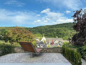 A bench overlooking a town with traditional architecture and a forested hill in the background.