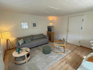 A living room with a sofa, a small round table, a chair, a lamp, and a door.