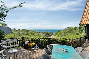 Eine Holzterrasse mit Tisch und Stühlen, einer Bank und Blick auf das Meer.