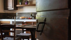 Een keuken met een houten tafel, stoelen, een brood, tomaten, een wijnfles en een potplant.