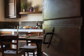 A kitchen with a wooden table, chairs, a bread loaf, tomatoes, a wine bottle, and a potted plant. - Apartment in Agriturismo with wellness in Maremma (Massa Marittima)
