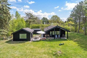 A modern house with a patio, a covered outdoor seating area, and a lawn. - Family oasis near nature, beach & Sommerland (Højby)