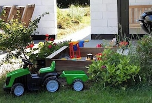 A garden with a green tractor, wooden chairs, and a wooden bench. - Family oasis near nature, beach & Sommerland (Højby)