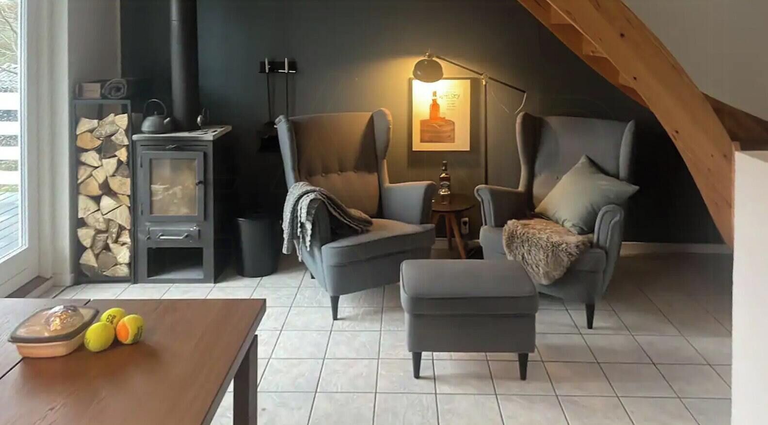 En hyggelig stue med pejs, to lænestole, et lille bord med kugler og en lampe.