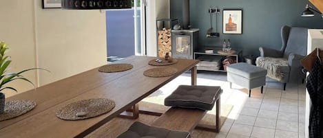 A dining area with a long wooden table, cushioned benches, a fireplace, and a view of the outdoors.