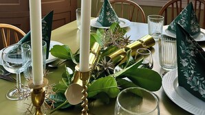 Mesa de jantar posta com velas, copos e folhagem decorativa.