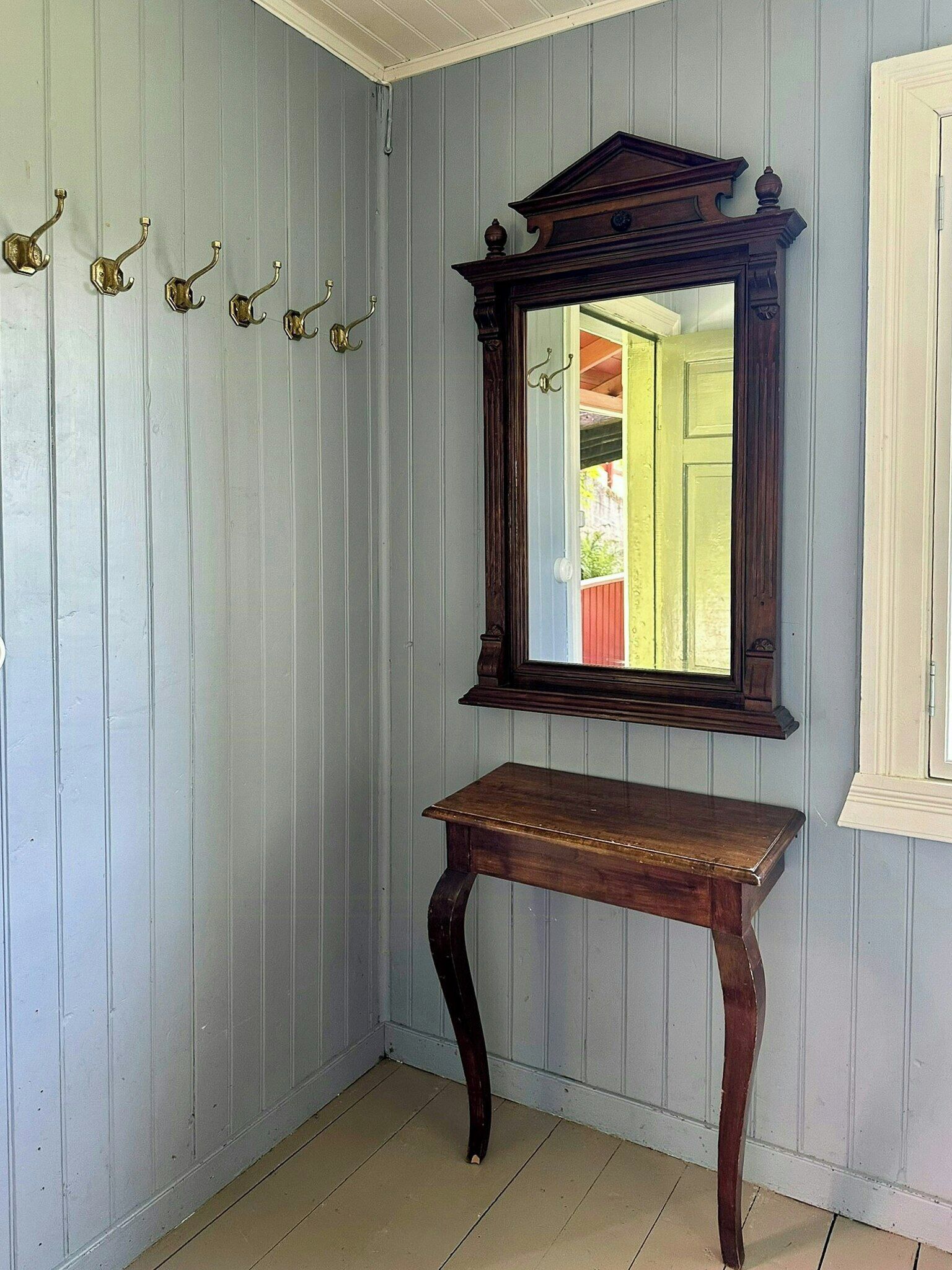 A room with a wooden console table and a mirror above it, against a light blue wall with vertical paneling.