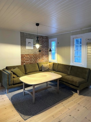 A living room with a green sofa, a wooden coffee table, a brick wall, and two windows. - Charming farmhouse from 1919 near Kristiansund (Kristiansund)