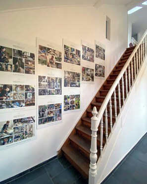Una escalera con barandal de madera y una pared decorada con varias fotografías enmarcadas.