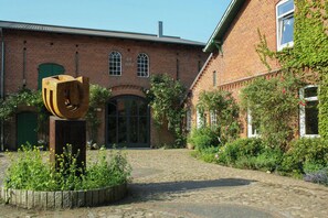 Un patio con un edificio de ladrillo, una escultura de madera y un jardín con diversas plantas.