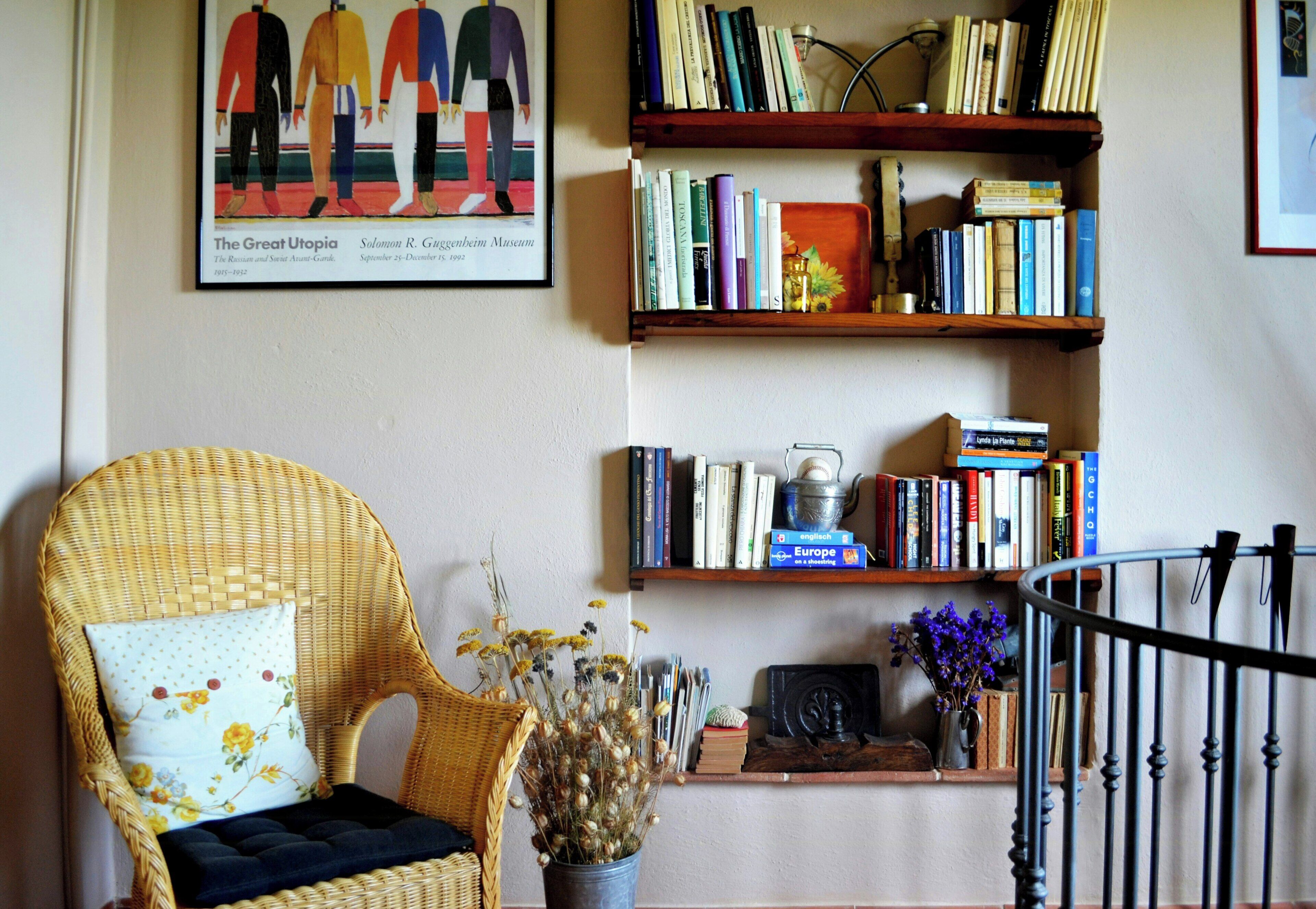 Une pièce avec un fauteuil en osier, une bibliothèque et un tableau encadré accroché au mur.