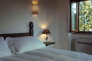 Ein Hotelzimmer mit einem Bett, einer Wandlampe, einem Nachttisch und einem Fenster mit Blick auf Bäume.