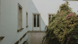 Uma viela estreita com um edifício de um lado e uma árvore com flores cor-de-rosa do outro.