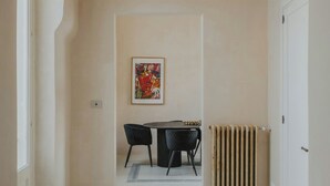 Um corredor com um radiador, uma obra de arte emoldurada na parede e um espaço de jantar com cadeiras e uma mesa.