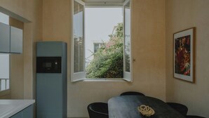 Quarto com mesa de jantar, cadeiras, micro-ondas, janela com vista para áreas verdes e um quadro na parede.