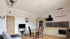 A modern living room with a sofa, dining table, chairs, and a kitchen area with cabinets and appliances. - Apartment in villa with shared pool in Razac (Razac-sur-l'Isle)