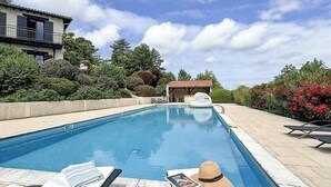 A swimming pool with lounge chairs and a sun umbrella, surrounded by greenery and a building in the background. - Apartment in villa with shared pool in Razac (Razac-sur-l'Isle)