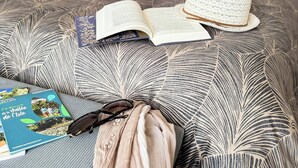 A neatly made bed with a patterned bedspread, an open book, a hat, and a pair of glasses on the bed. - Apartment in villa with shared pool in Razac (Razac-sur-l'Isle)