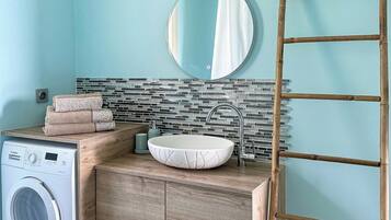 A bathroom with a washing machine, a sink with a white basin, a mirror, and a bamboo ladder.