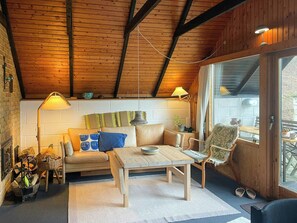 Ein gemütliches Zimmer mit Holzbalkendecke, einer Couch, einem Tisch und einem Stuhl.