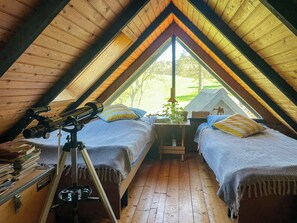 Ein gemütliches Schlafzimmer im Dachgeschoss mit zwei Betten, einem Teleskop und Blick ins Freie.
