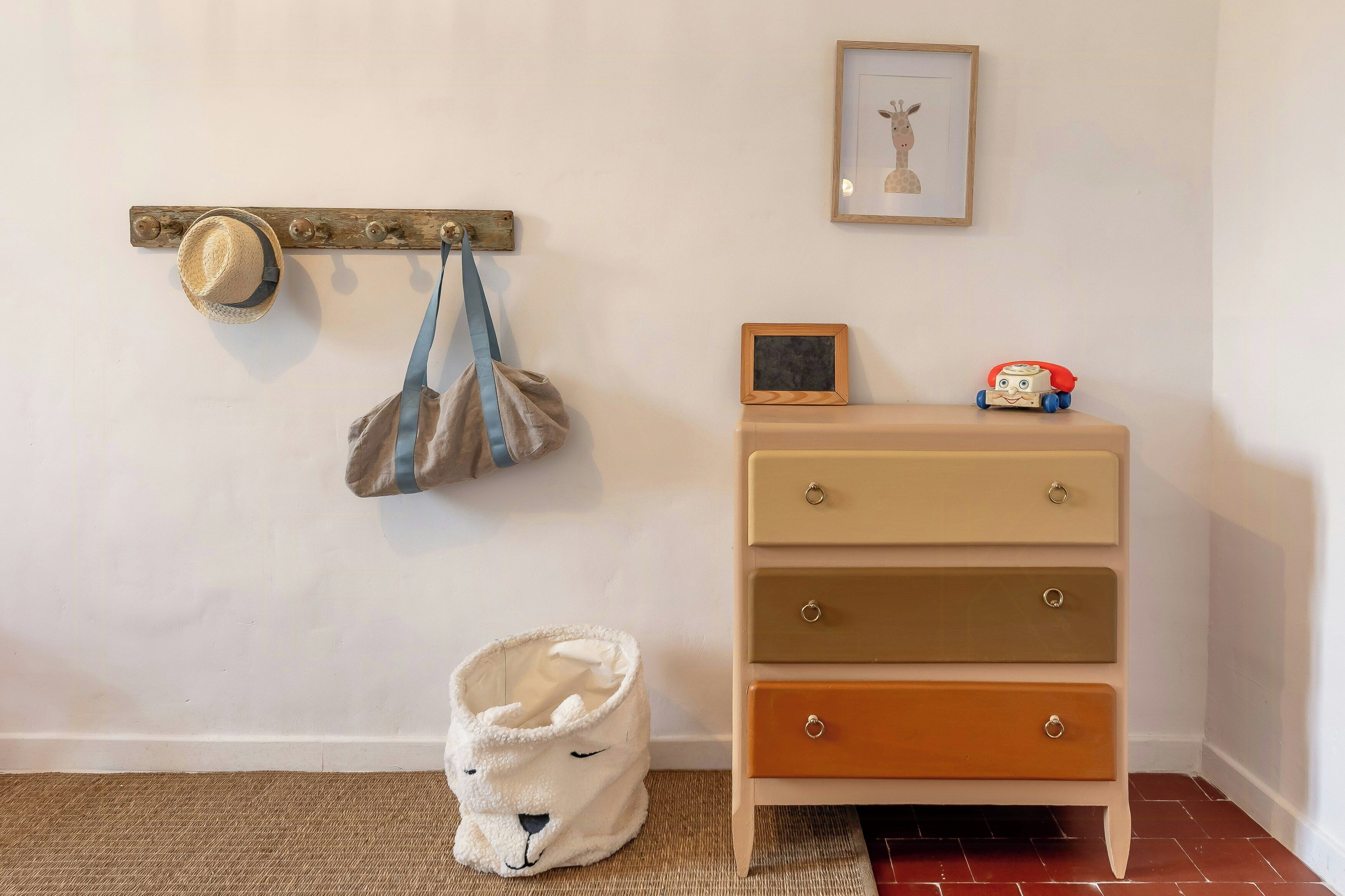 A room with a wooden coat rack, a framed picture, a dresser with drawers, and a white animal-shaped bag.