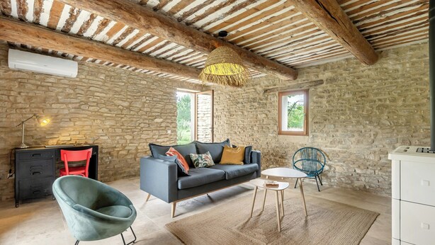 A rustic room with a stone wall, a sofa, a chair, a small table, and a hanging light fixture. - House with private beach on the Sorgue (L'Isle-sur-la-Sorgue)
