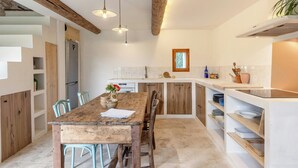 A kitchen with a wooden table, chairs, and a built-in island with a sink and storage. - House with private beach on the Sorgue (L'Isle-sur-la-Sorgue)