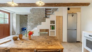 A kitchen with a rustic wooden table, a stone wall, a built-in bookshelf, and a stainless steel refrigerator. - House with private beach on the Sorgue (L'Isle-sur-la-Sorgue)