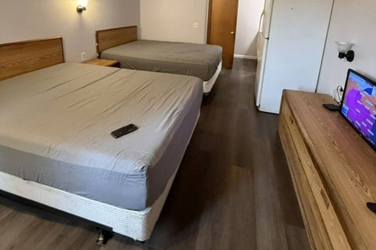 Una habitación de hotel con dos camas, un aparador de madera, un televisor y un refrigerador.