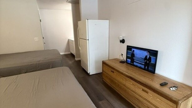 A hotel room with a bed, a television, a wooden dresser, and a refrigerator. - The Village Motel (Cambridge)