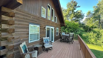 A wooden cabin with a deck, outdoor seating, and a view of the surrounding forest.