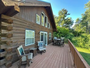 A wooden cabin with a deck, outdoor seating, and a view of the surrounding forest.