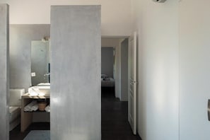 Ein modernes Badezimmer mit einem großen Spiegel, einem Waschbecken und einer Toilette. Ein Handtuchhalter mit Handtüchern ist vorhanden.