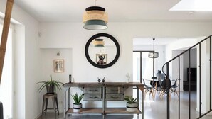 Cozinha moderna com mesa de madeira, duas plantas em vasos, luminária pendente e espelho redondo na parede.