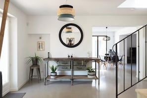 Eine moderne Küche mit einem Holztisch, zwei Blumentöpfen, einer Hängelampe und einem runden Spiegel an der Wand.