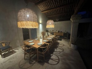 Ein Essbereich mit einem langen Holztisch, Körbe-Pendelleuchten und einer Küche im Hintergrund.
