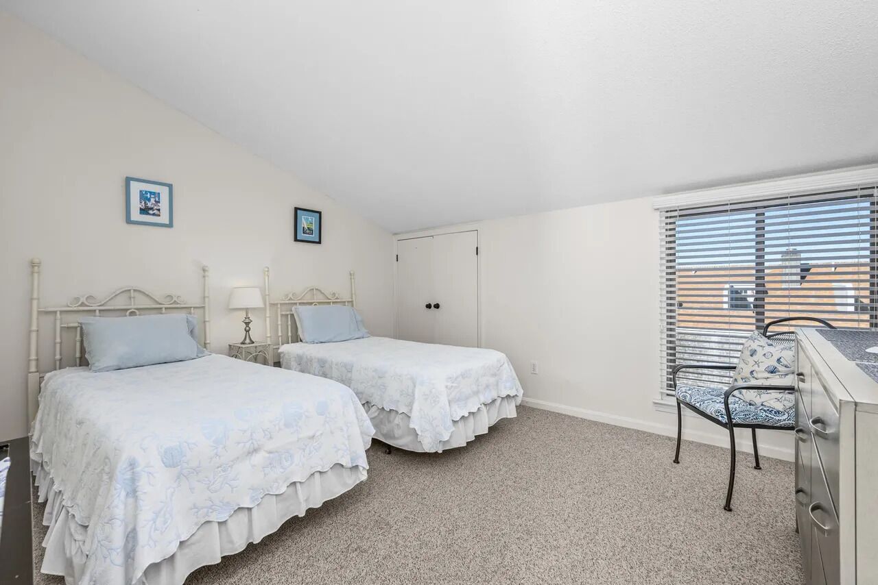 Une chambre avec deux lits, un bureau, une chaise et une fenêtre avec des stores.