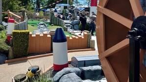 Un terrain de jeux doté d’une grande roue en bois, d’une décoration en forme de fusée et d’une structure en forme de phare.