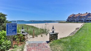 Une plage avec un panneau indiquant les règles à respecter sur cette plage privée, un sentier en pierre et une rangée de maisons en arrière-plan.