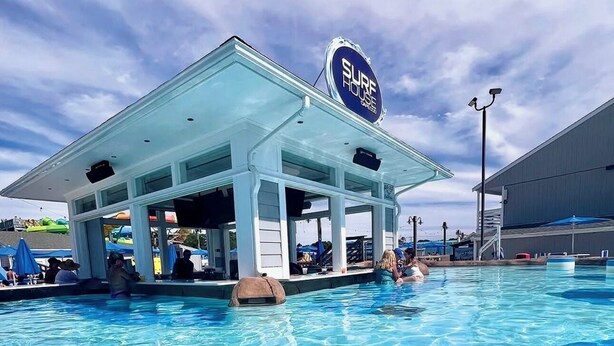 Un espace piscine doté d’un coin salon abrité et d’un panneau indiquant « SURF HOUSE ».