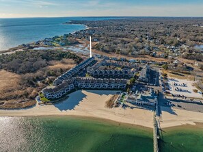 An aerial view of a coastal residential area with a row of houses, a beach, and a pier.