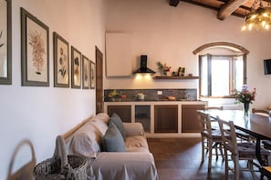 Eine gemütliche Küche mit Einbauherd, ein Essbereich mit Holztisch und -stühlen sowie eine Sitzecke mit Sofa und Korbwannenmöbel.