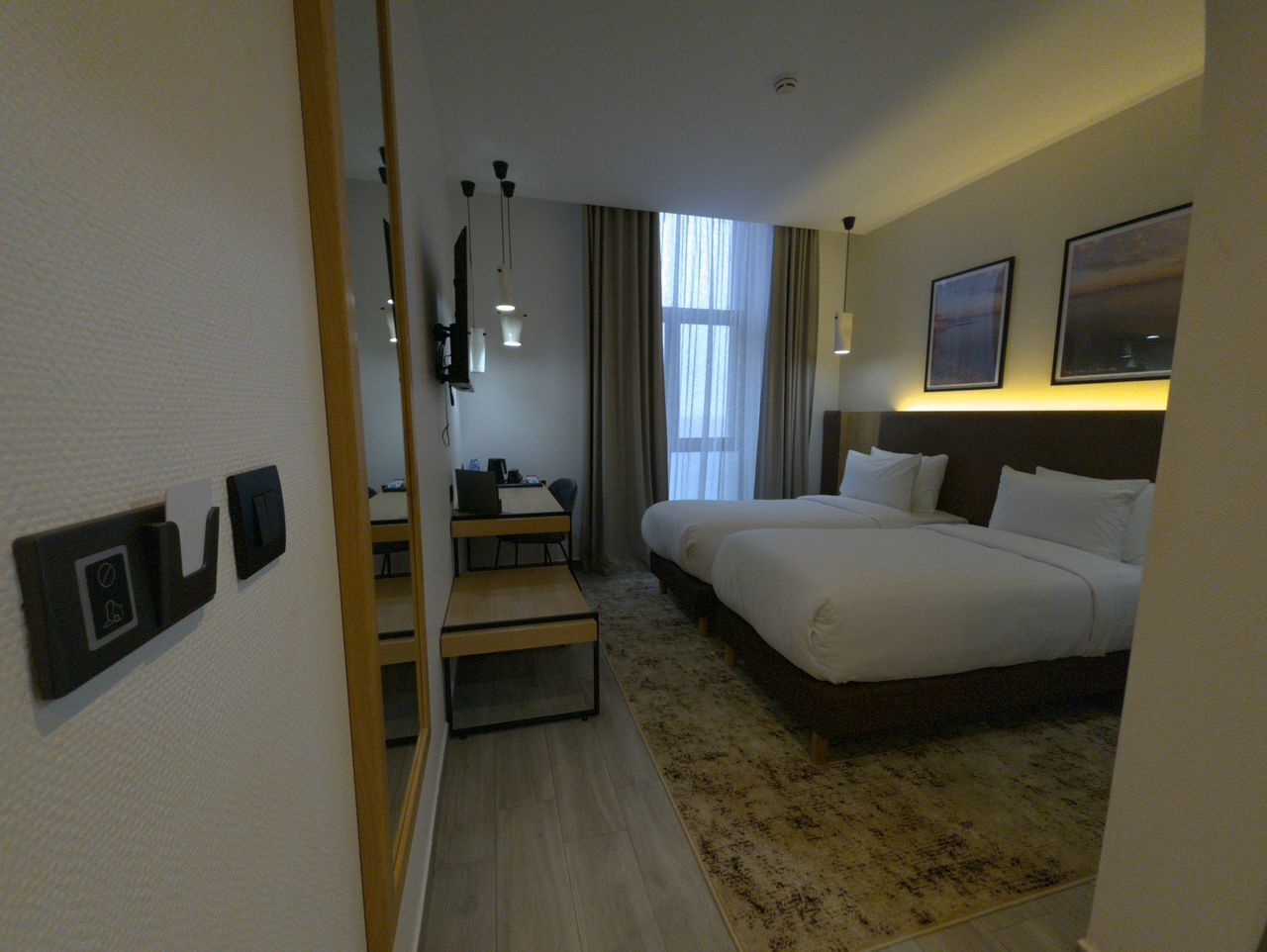 A hotel room with a bed, a desk, a chair, a small table, and a mirror.