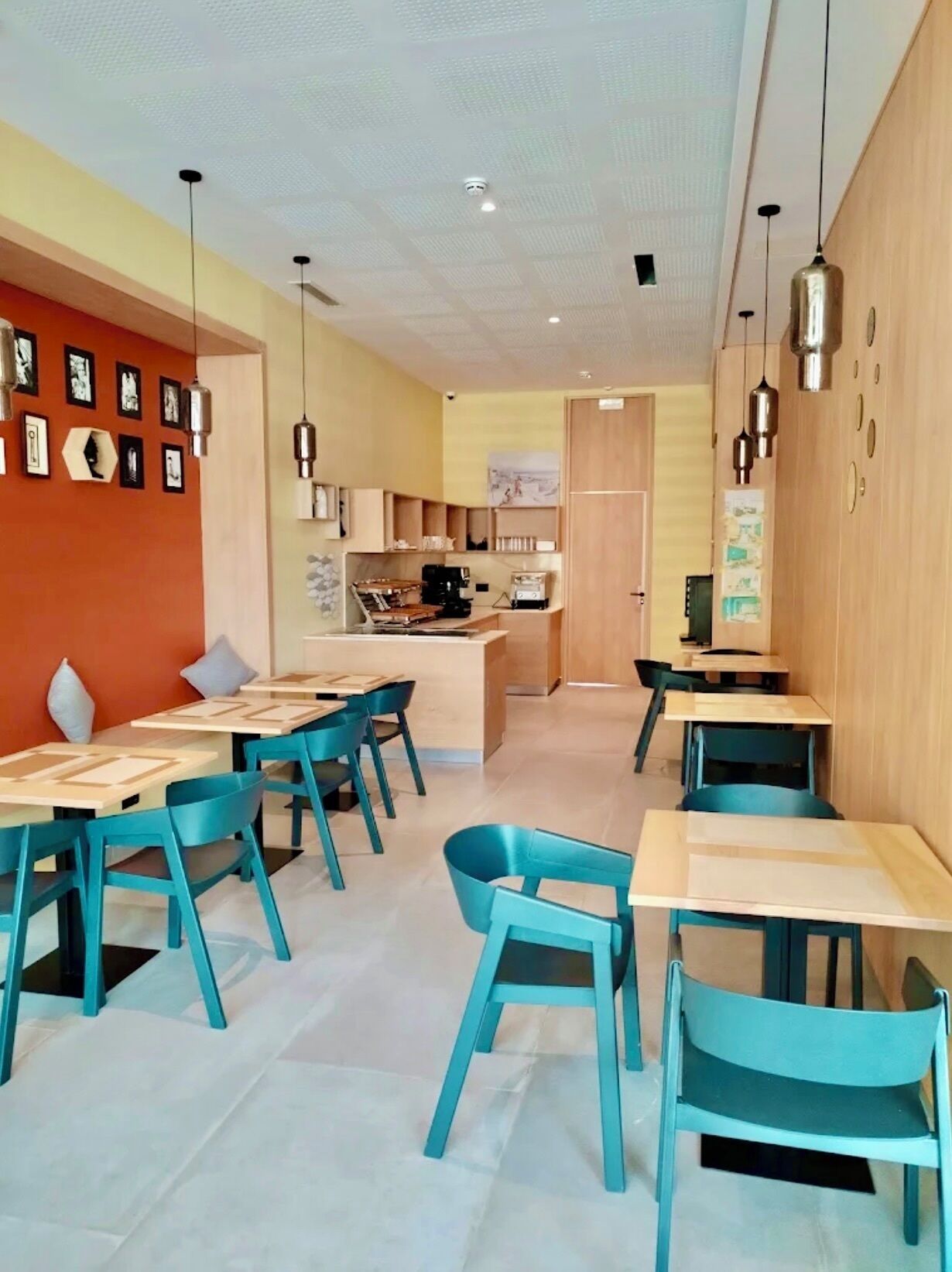 Un comedor moderno con sillas y mesas color turquesa, una cocina al fondo y un techo con diseño de cuadrícula.