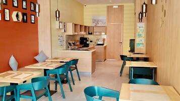 Un comedor moderno con sillas y mesas color turquesa, una cocina al fondo y un techo con diseño de cuadrícula.